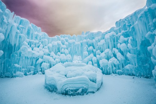 A stunning ice cave with towering blue ice formations and a central frozen structure under a colorful sky.