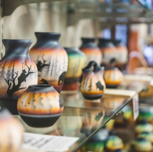 A display of colorful pottery vases featuring nature scenes with trees and wildlife, arranged on glass shelves.