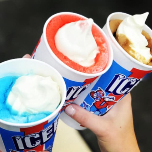 Three colorful ice cream cups with whipped cream, held in one hand: blue, red, and brown flavors.