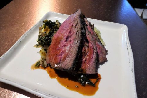 A plate of sliced beef brisket served over greens with a rich sauce, presented on a white dish.