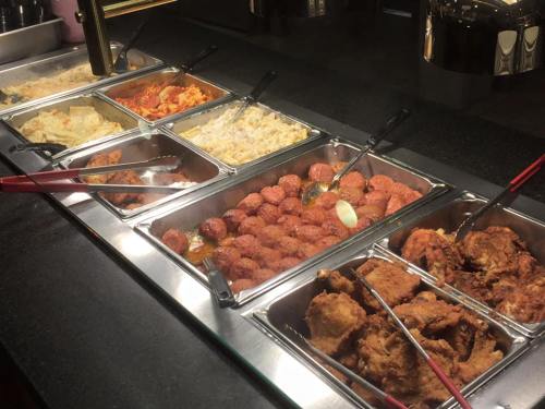 A buffet with various dishes, including fried chicken, meatballs, rice, and pasta, all in metal serving trays.