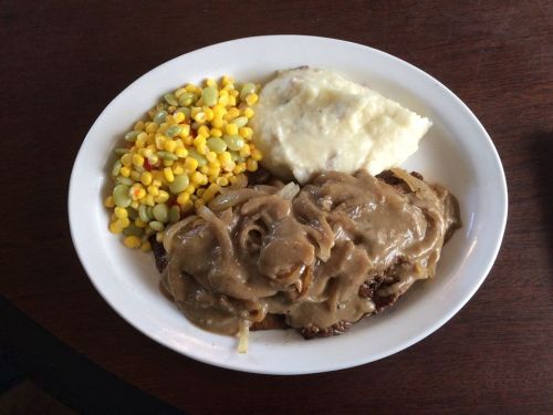 A plate of food featuring mashed potatoes, corn, and meat covered in gravy with onions.