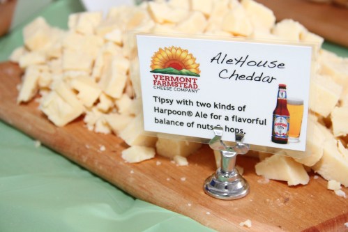 A wooden board with chunks of cheese labeled "AleHouse Cheddar" and a sign about its flavor profile with beer.