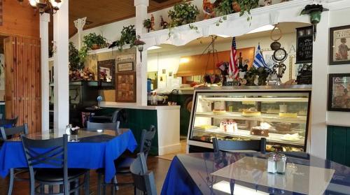 Cozy café interior with blue tablecloths, a dessert display case, and decorative plants on the walls.
