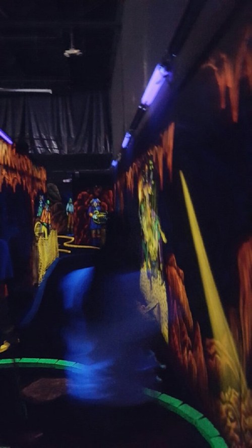 A dimly lit hallway with glowing murals and a winding path, creating a vibrant, immersive atmosphere.