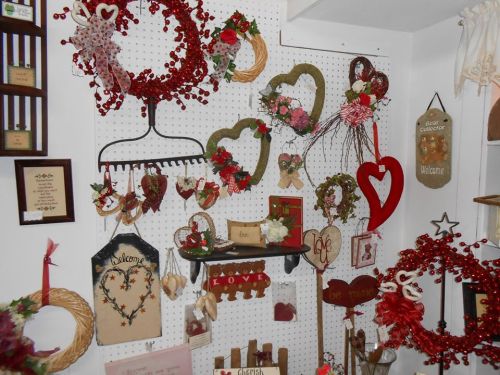 A display of decorative wreaths and signs in heart shapes, featuring flowers and welcoming messages on a pegboard.