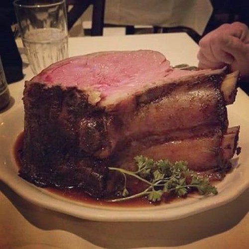 A large, juicy roast beef on a plate, garnished with parsley, served in a restaurant setting.