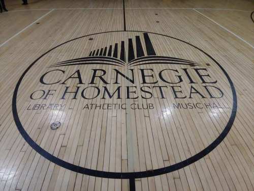 Logo of Carnegie of Homestead featuring a stylized book and text on a wooden gym floor.