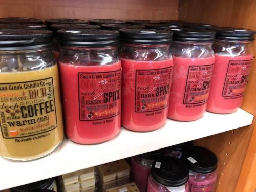 A shelf displaying various scented candles in jars, including coffee and dark spice fragrances.