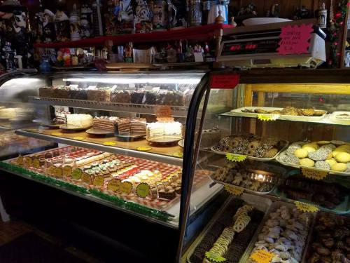 A display case filled with various cakes, cookies, and pastries, labeled with colorful tags in a cozy bakery setting.