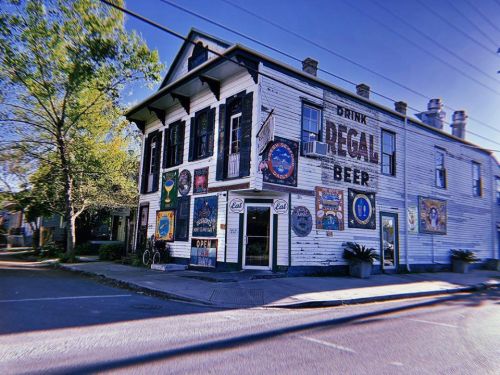 A vintage two-story building with colorful beer advertisements and a tree in front, set on a quiet street.