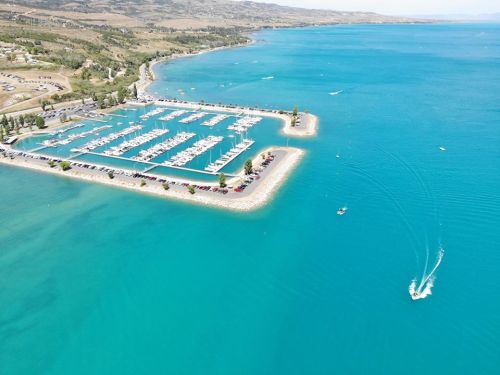 Aerial view of a marina with boats, surrounded by turquoise water and green hills in the background.