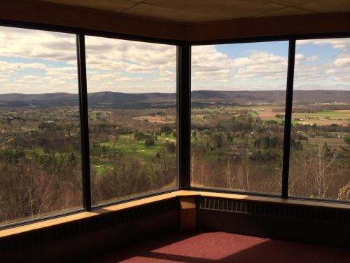A panoramic view of rolling hills and fields through large windows, with a blue sky and clouds above.