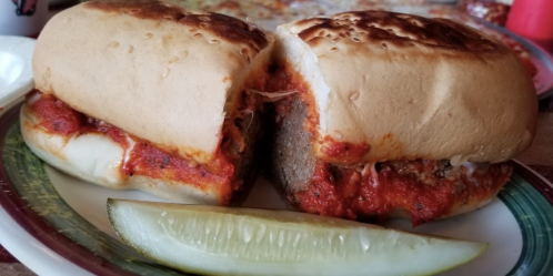 Two meatball sandwiches with marinara sauce, served on a plate with a pickle slice.