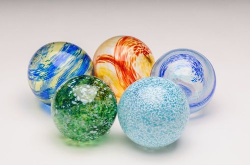 Five colorful glass spheres with various patterns and textures arranged on a light background.