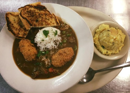 A plate of gumbo with rice, fried chicken, toast, and a side of potato salad.