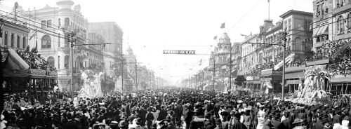 A crowded street during a parade, with ornate buildings and decorations, in a historic black-and-white photograph.