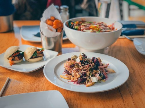 A plate of colorful salad with vegetables and toppings, alongside bao buns and a bowl of noodles in the background.