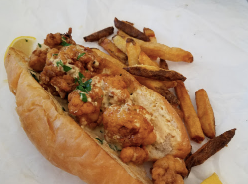 A sandwich filled with crispy fried cauliflower and sauce, served with a side of golden French fries.