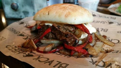 A hearty sandwich filled with grilled steak, sautéed onions, and red peppers on a soft bun, served on parchment paper.