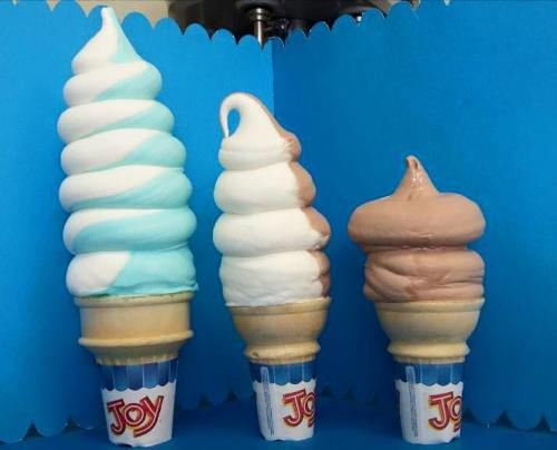 Three soft serve ice cream cones in blue, white, and brown flavors, displayed against a blue background.