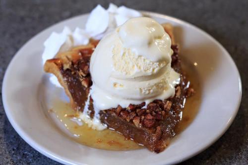 A slice of pie topped with vanilla ice cream and chopped nuts, served with whipped cream on a plate.
