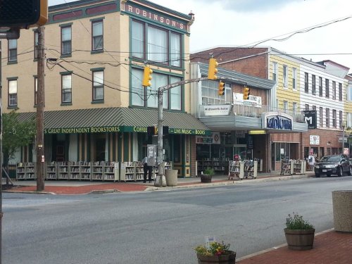 A street view featuring independent bookstores, coffee shop, and shops with colorful awnings in a small town.