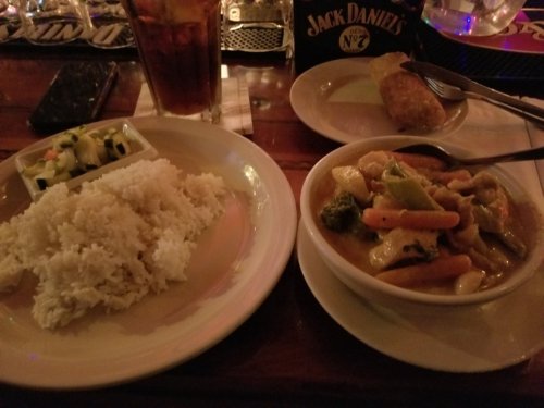 A plate of rice, a vegetable curry with chicken, a spring roll, and a small salad on a wooden table.