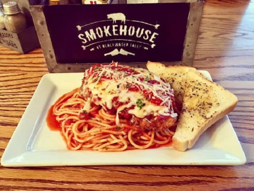 A plate of spaghetti topped with marinara sauce and cheese, served with garlic bread, in front of a "Smokehouse" sign.
