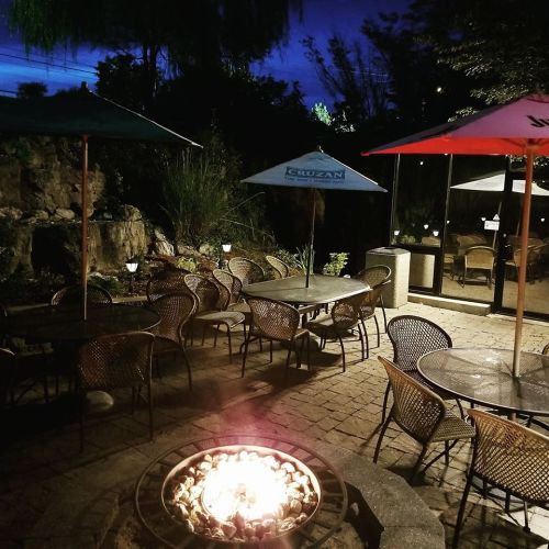 Cozy outdoor seating area with tables, umbrellas, and a fire pit, illuminated at night with a dark blue sky.