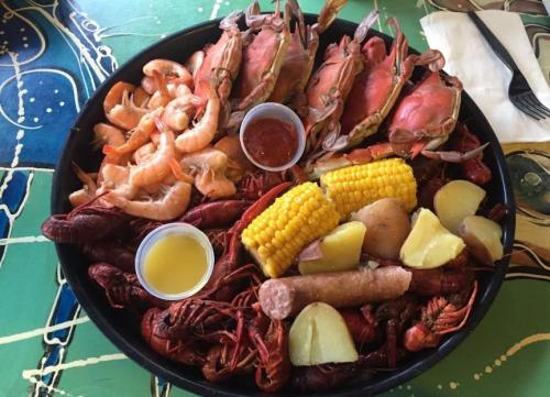 A seafood platter featuring shrimp, crabs, crawfish, corn, potatoes, and dipping sauces on a colorful table.