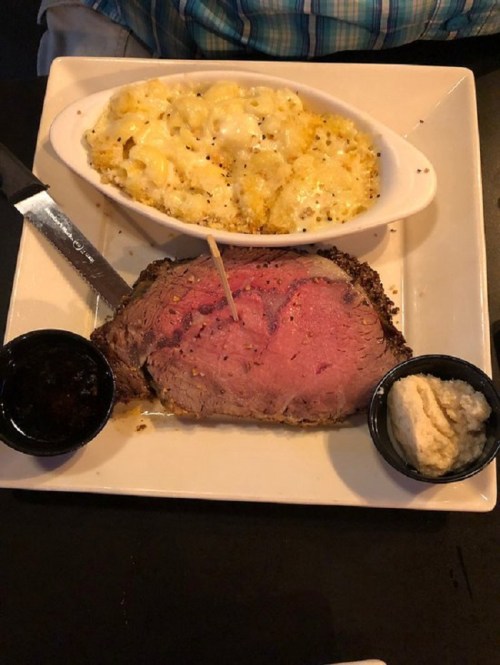 A plate featuring a slice of prime rib with a toothpick, macaroni and cheese, and two sauces on the side.