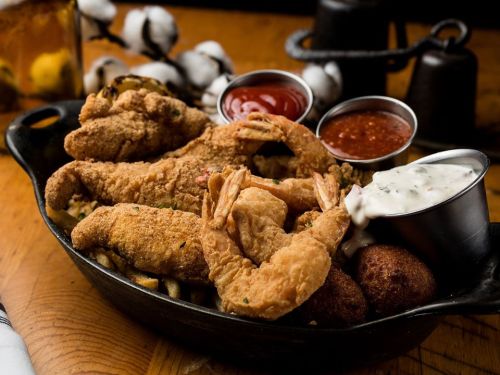 A platter of fried shrimp with dipping sauces and hushpuppies, served in a cast iron skillet.
