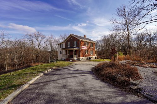 A two-story brick house with a "Mason" sign, surrounded by trees and a winding driveway on a sunny day.