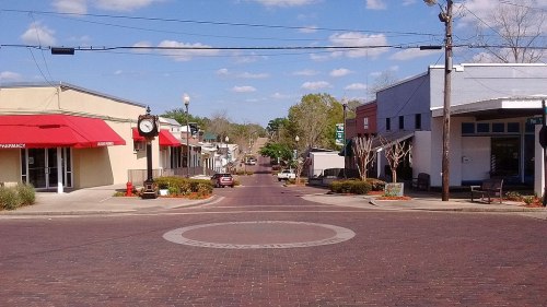 A quiet street view of a small town with shops, a clock, and trees under a blue sky with scattered clouds.