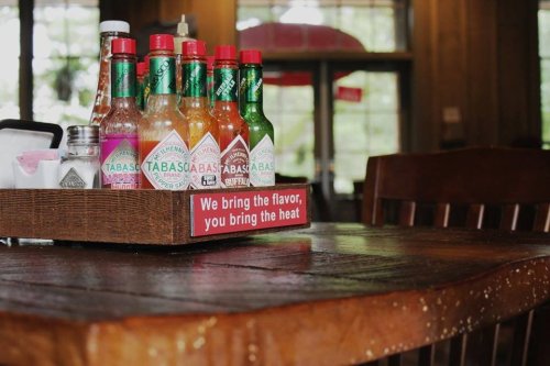 A wooden table with a tray of various Tabasco hot sauces and a sign that reads, "We bring the flavor, you bring the heat."