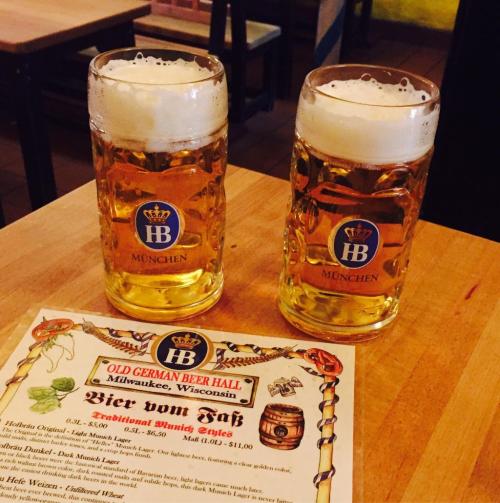 Two glasses of beer with frothy tops sit beside a menu from the Old German Beer Hall in Milwaukee, Wisconsin.