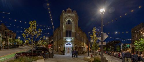 A charming building illuminated at night, surrounded by string lights and trees, with people gathered outside.