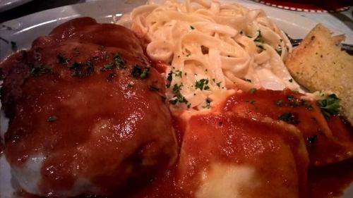 A plate of pasta with fettuccine, ravioli in marinara sauce, and a piece of garlic bread, garnished with parsley.