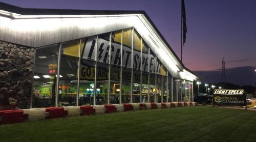 Exterior of Light Speed entertainment center at dusk, featuring large windows and a sign for escape chambers.