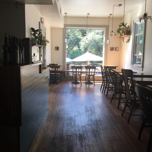 Cozy interior of a café with wooden floors, tables, and a large window overlooking an outdoor patio.