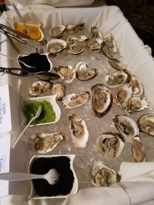 A display of fresh oysters on ice, accompanied by caviar, green garnish, and sauces in small bowls.