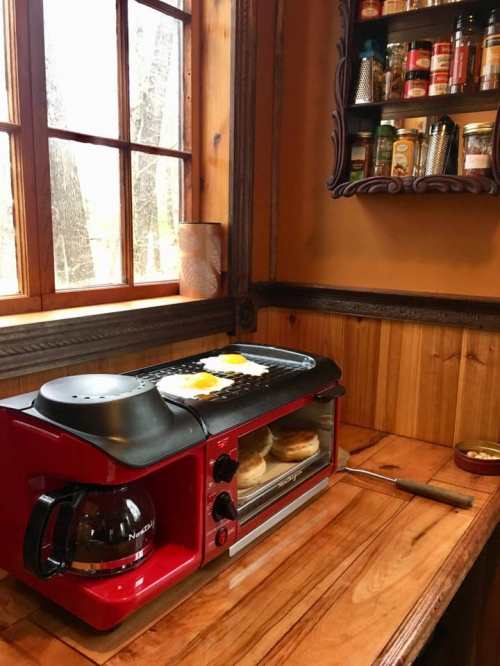 A red countertop appliance with a coffee maker and griddle, set in a cozy kitchen with wooden walls and shelves of spices.