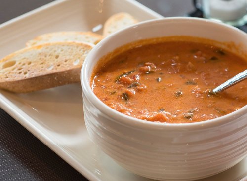 A bowl of tomato soup with spinach, served with slices of toasted bread on a white plate.