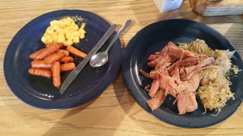 Two blue plates: one with macaroni and cheese, glazed carrots; the other with pulled pork and sauerkraut.