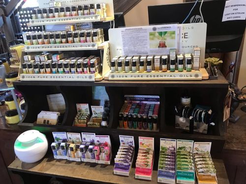 Display of various essential oils and related products on a wooden shelf in a store.