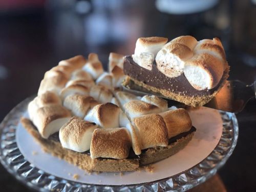 A chocolate pie topped with toasted marshmallows, partially sliced and served on a decorative plate.