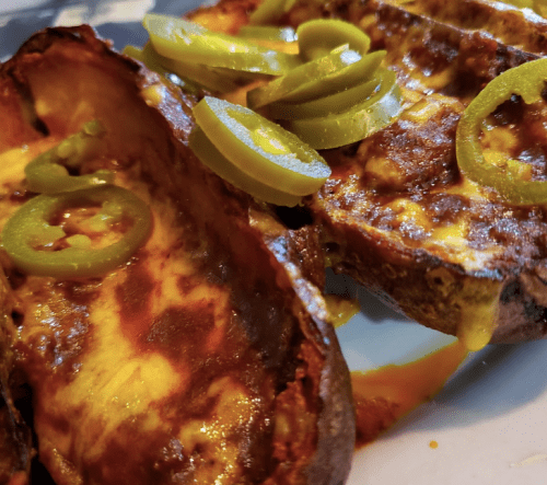 Baked potato halves topped with melted cheese and sliced jalapeños on a white plate.