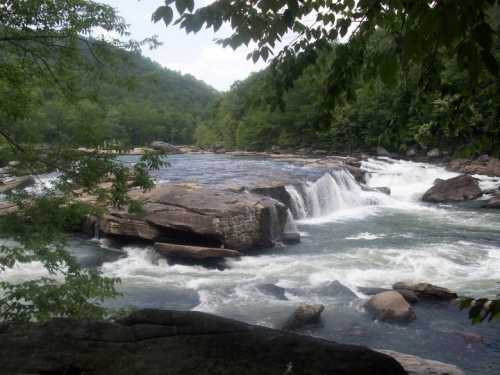 A serene river scene with cascading waterfalls surrounded by lush green trees and rocky formations.