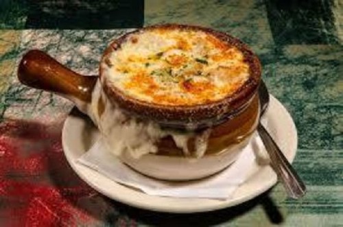 A bowl of French onion soup topped with melted cheese, served on a plate with a spoon.